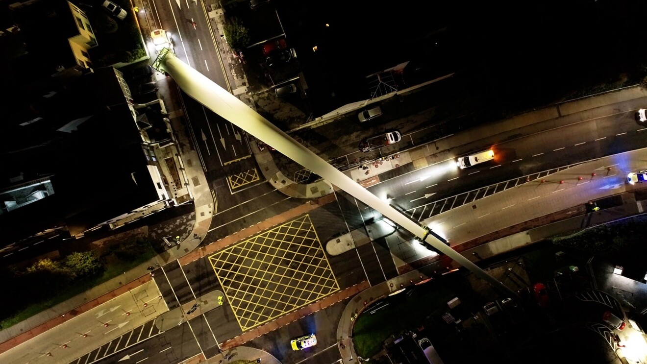 An aerial photo of a wind turbine blade being transported on a highway.