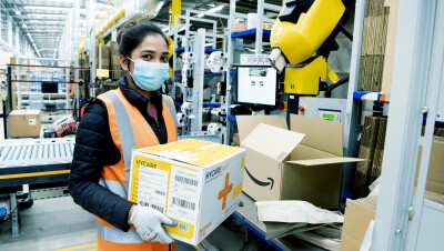 An Amazon employee at Coalville fulfillment center packs boxes with medical supplies to be sent to relevant government centers. She is wearing protective gloves and a face mask. 