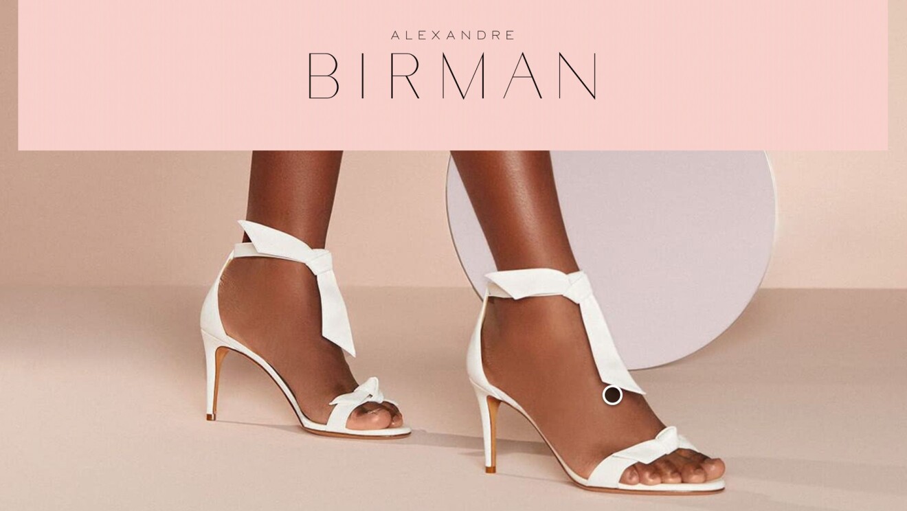 An image that shows white heels worn by a model and text that reads "Alexandre Birman" at the top.