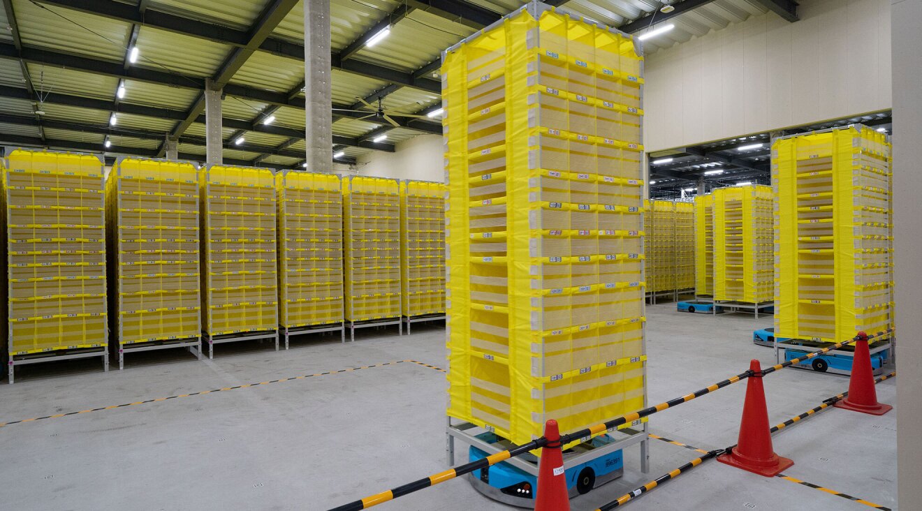 倉庫の中に黄色い棚が数十個並んでいる。そのうちのいくつかの棚の下に青いロボットが設置されている
