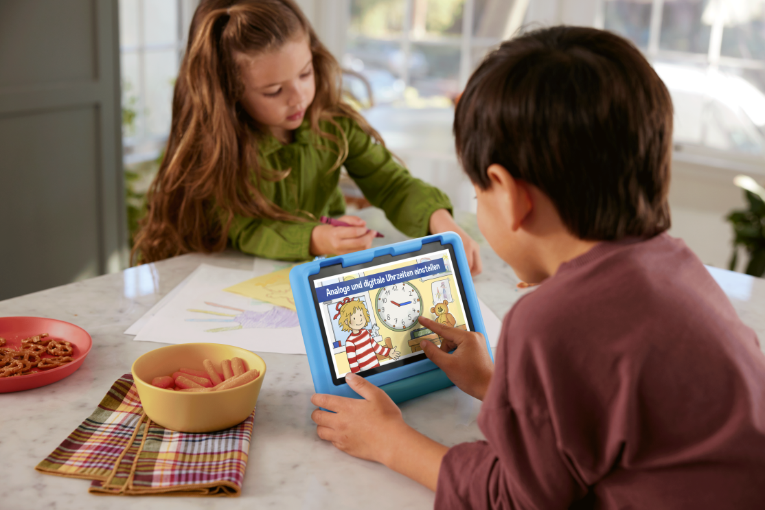 Eine kleiner Junge ist an einem Tisch und nutzt ein Tablet mit blauer Hülle.