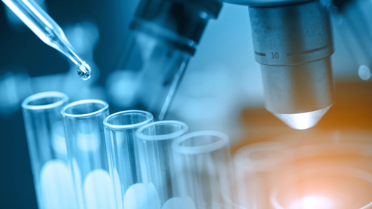A microscope, test tubes, and a pipette with a drop of liquid emerging.