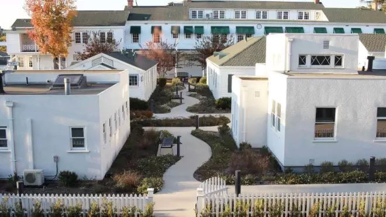 個人の家のようなそれぞれデザインが異なる白い建物が4つ並ぶ向こう側に窓がたくさんついた大きな建物が見える