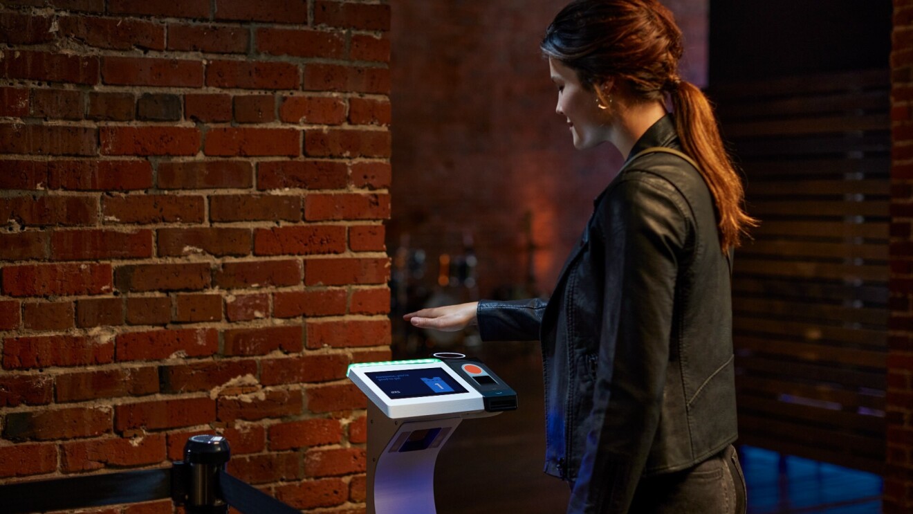 A woman holds her palm over a Amazon One device at a concert venue.