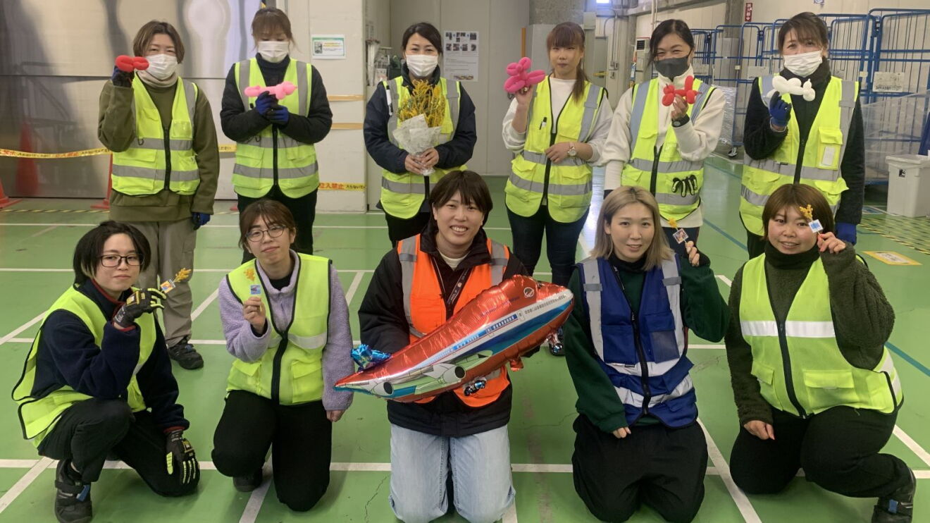 飛行機の風船や花などを持っている数人の女性たち。彼女たちは持っている物を見せている。