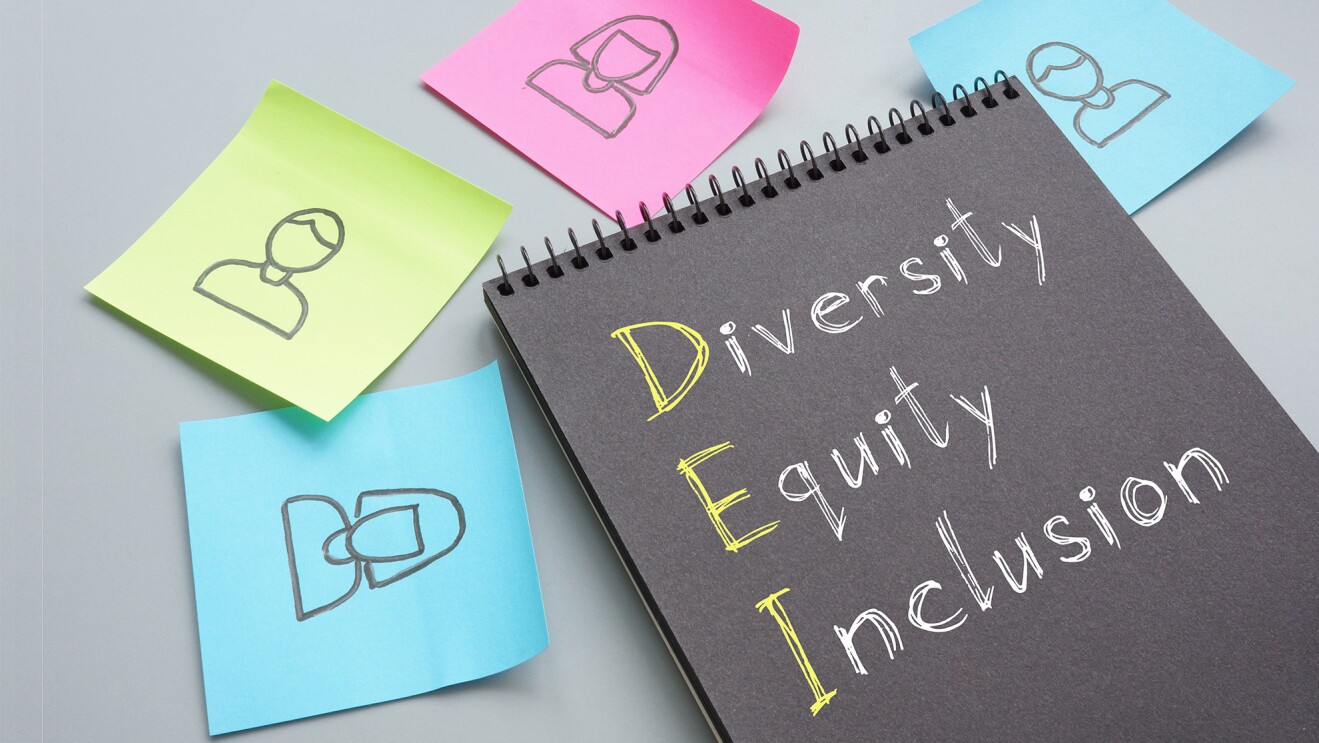 付箋紙に書かれた人物のイラストと黒いノートの表紙に書かれたDiversity Equity Inclusionの文字