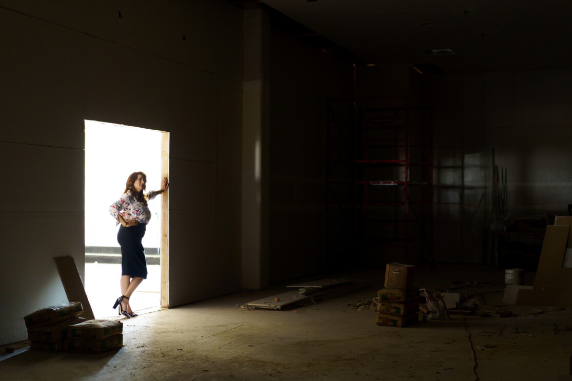 A woman stands in a doorway looking into a large room that appears to be in the final stages of construction.