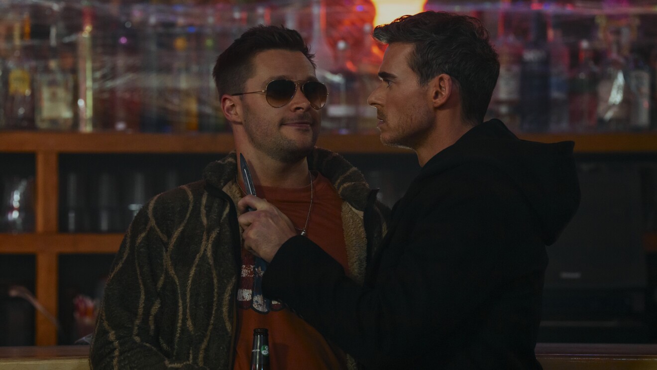 Citadel S2: Two men talking at a bar, one wearing sunglasses and a patterned jacket, the other in all black