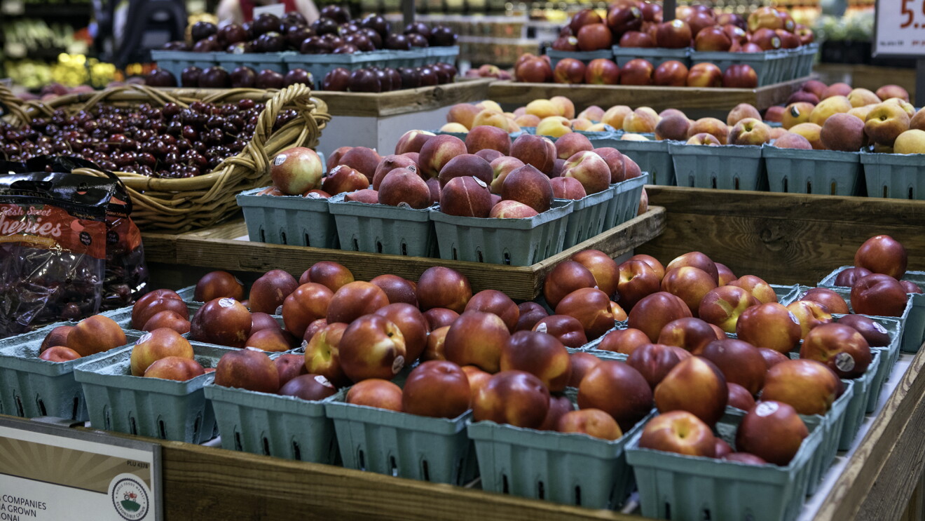 Produce displayed in a Whole Foods Market store - nectarines, cherries, and peaches are in the foreground, with a refrigerated juice display behind it. 
