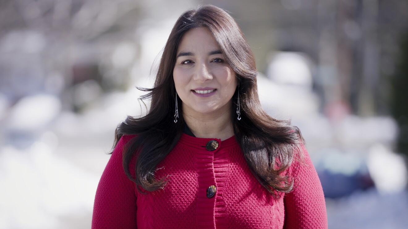 一个女人在一个红色的温文尔雅的毛衣站对着镜头微笑。背景是模糊的。