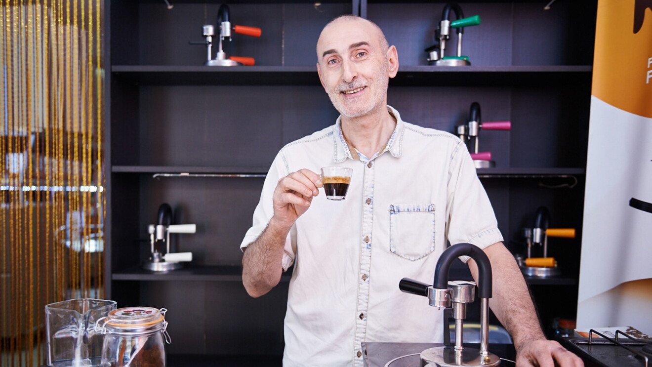 Nino Santoro, l'inventore di Kamira, regge una tazzina di espresso e mostra orgoglioso la sua macchina accanto a una brocca d'acqua e un vaso di polvere di caffé