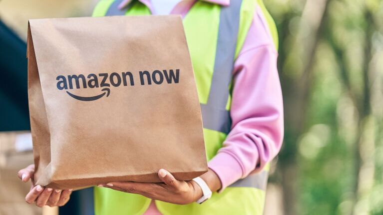Delivery person in reflective vest holding Amazon Now paper bag