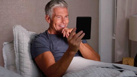 Man in bed reading on his Kindle.