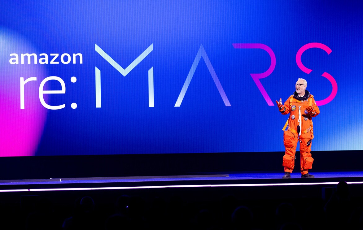 An image of a man standing on the re:MARS stage in an orange space suit.