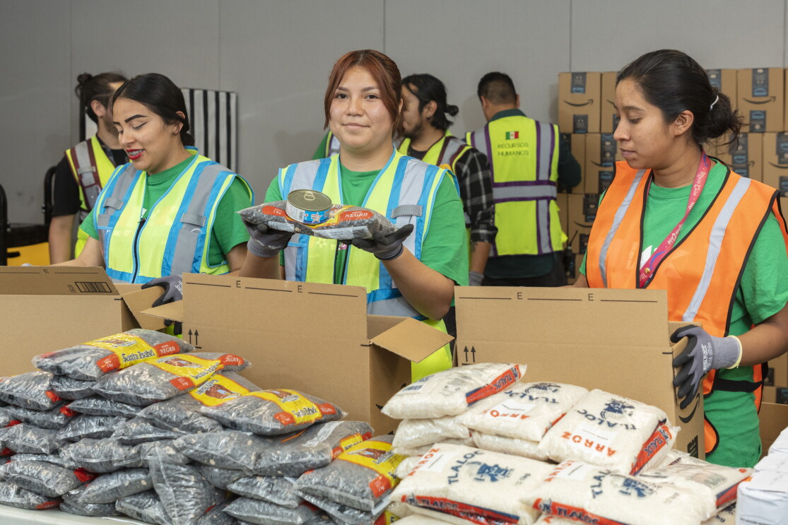 Tres mujeres con chalecos preparando comida para poner en cajas de ayuda ante emergencias. 