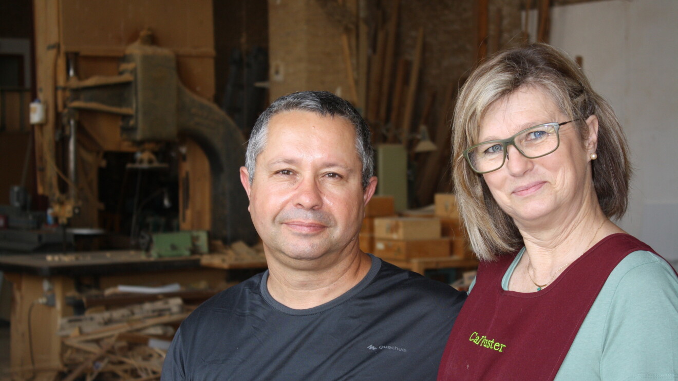 Josep Veciana y Lydia-Bárbara Plazas son una pareja de Barberá de la Conca. De fondo tienen su carpintería. Ella, con gafas, luce un delantal, él una camiseta deportiva. 

