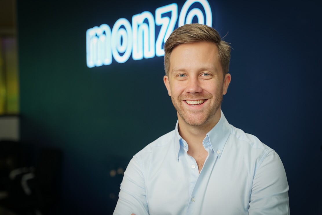 Tom Blomfield from Monzo looking directly at the camera and smiling against a blue background and Monzo logo