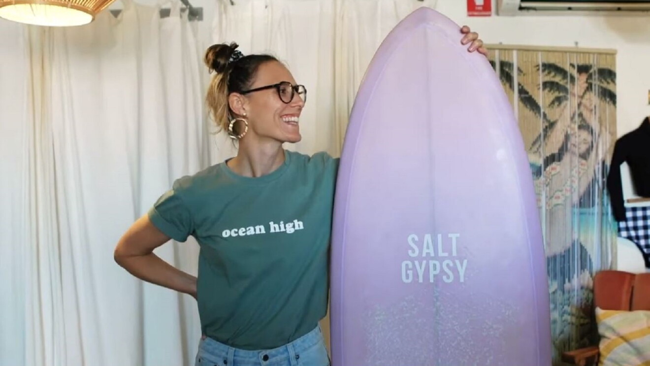 Salt Gypsy’s founder Danielle Clayton holding a surfboard in her shop