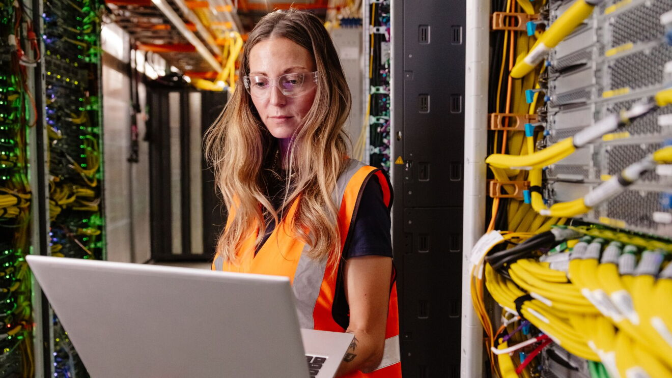 A female data center technician using a laptop to work inside a data center facility