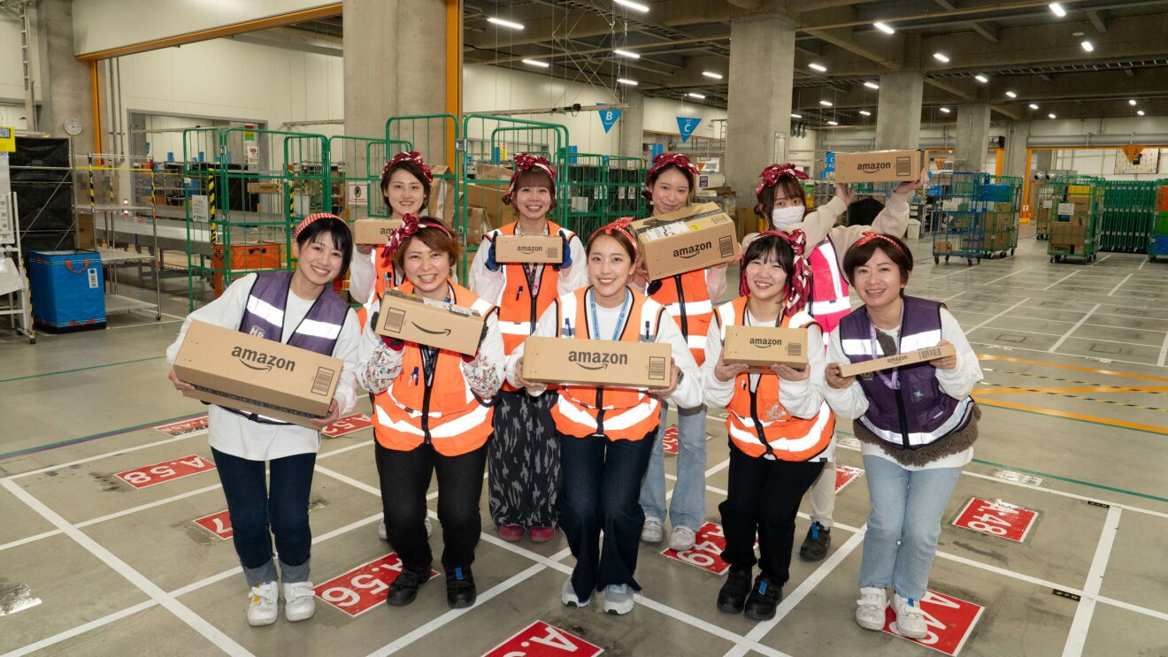作業用のベストを着た数人の女性たちがAmazonボックスを持って集まっている