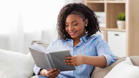 Une femme lit un livre gris chez-soi. 