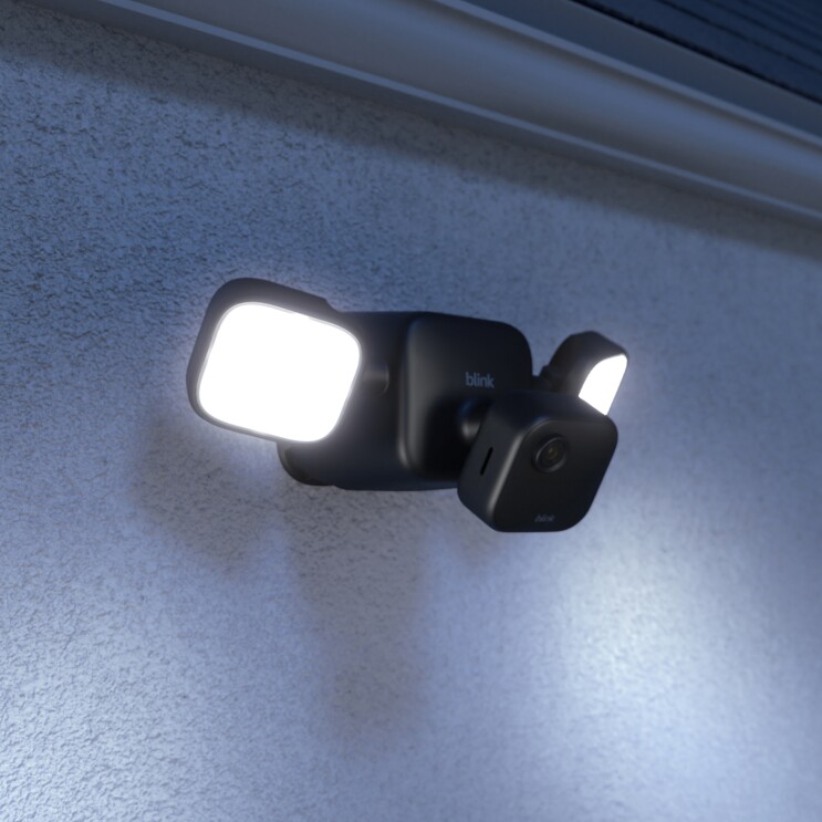 Die neue Blink Outdoor Floodlight Camera in Schwarz unter dem Dach auf eine Mauerwand eines Hauses befestigt.