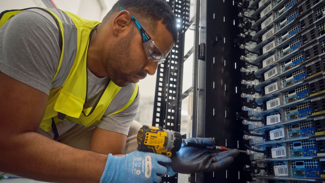 An employee using an electric power drill to work on a server rack.