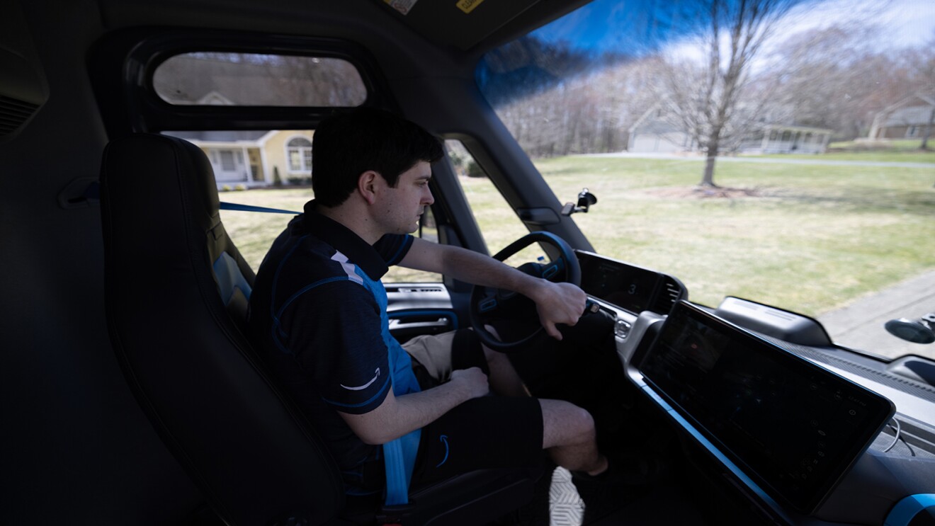 An amazon delivery driver drives a Rivian van.