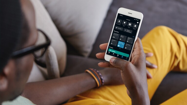 An image of a person wearing yellow pants looking at their phone screen. The focus of the image is the phone, which shows the Alexa app open.