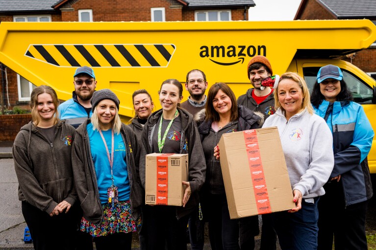 Volunteers stand in front of an Amazon Tonka-style truck delivering Christmas presents to children in need