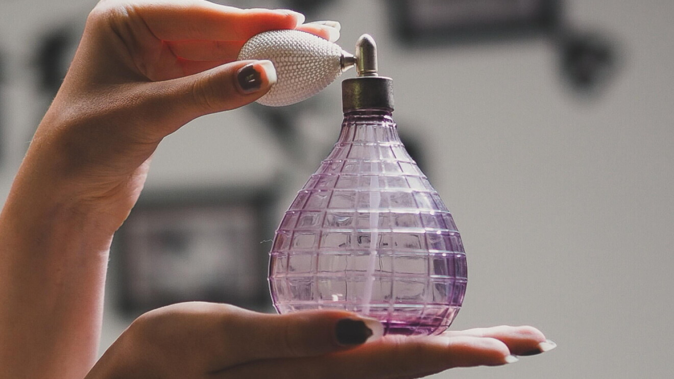 A woman with chipped nail polish squeezes the atomizer on a fragrance bottle.