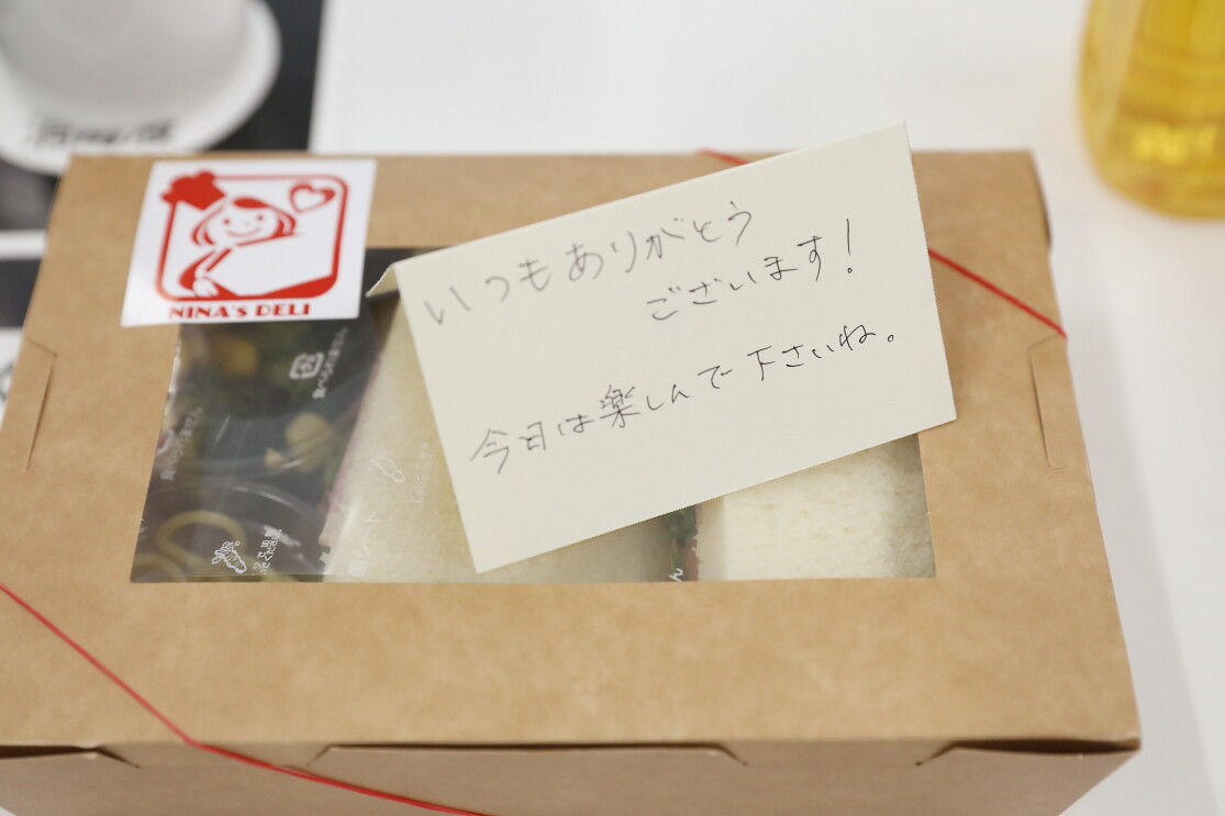 サンドイッチが入ったランチボックスに添えられたメッセージ「いつもありがとうございます。今日は楽しんでくださいね」