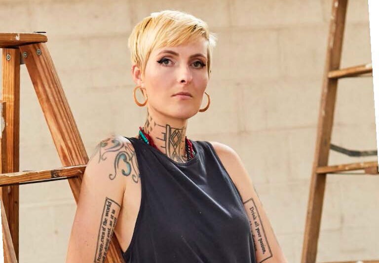 An image of Growlove standing for a photo while leaning on a wooden ladder. There is another ladder behind her.