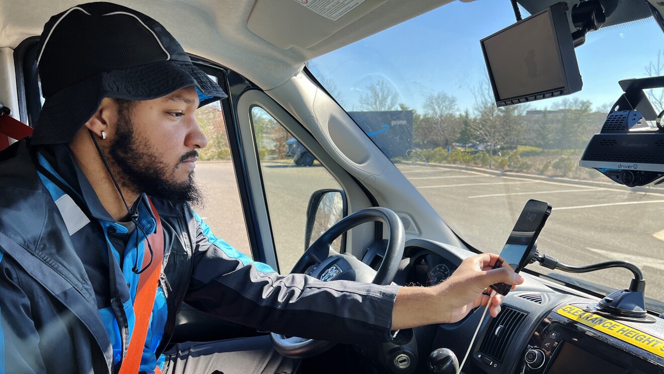 Torazz Richardson sits in the front seat of a delivery vehicle and looks at a smartphone attached to the dashboard.