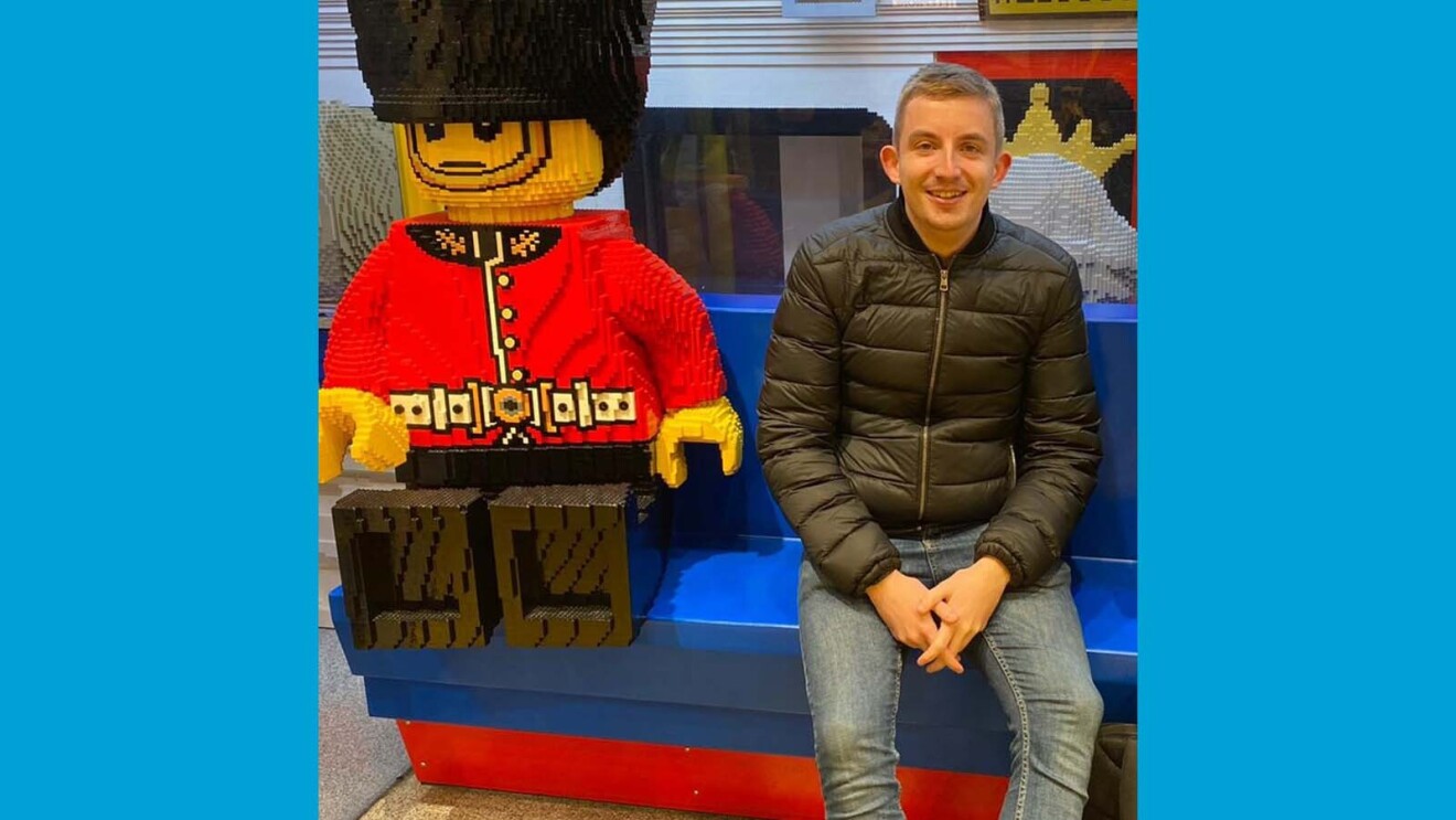 Luke smiling and sitting on a bench next to giant Lego statues at the Lego store in London.