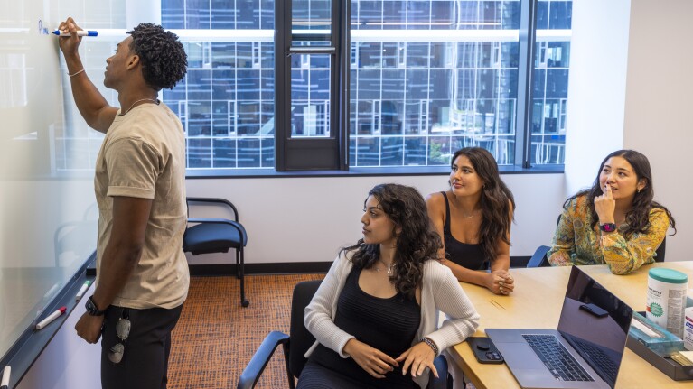 Four Amazon employees sit in a conference room while one writes on the whiteboard.