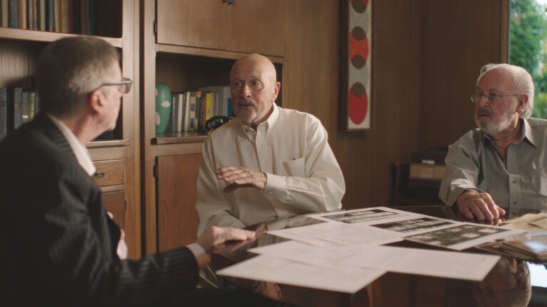 Three older men in discussion around a table with documents