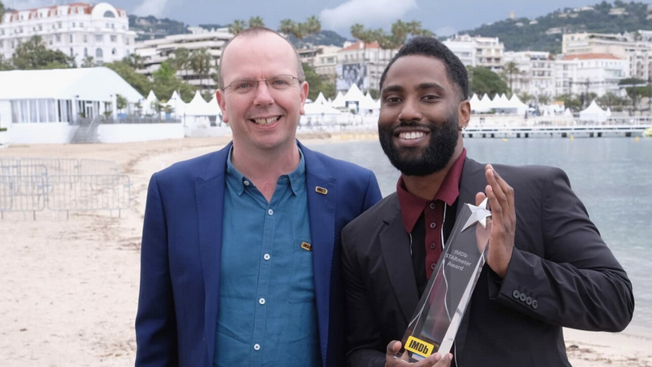 A photo of Col Needham, founder and CEO of IMDb standing next to John David Washington, who is holding an IMDb award.