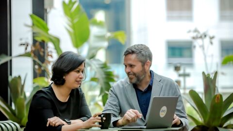 A man is pointing at a laptop while talking to a woman