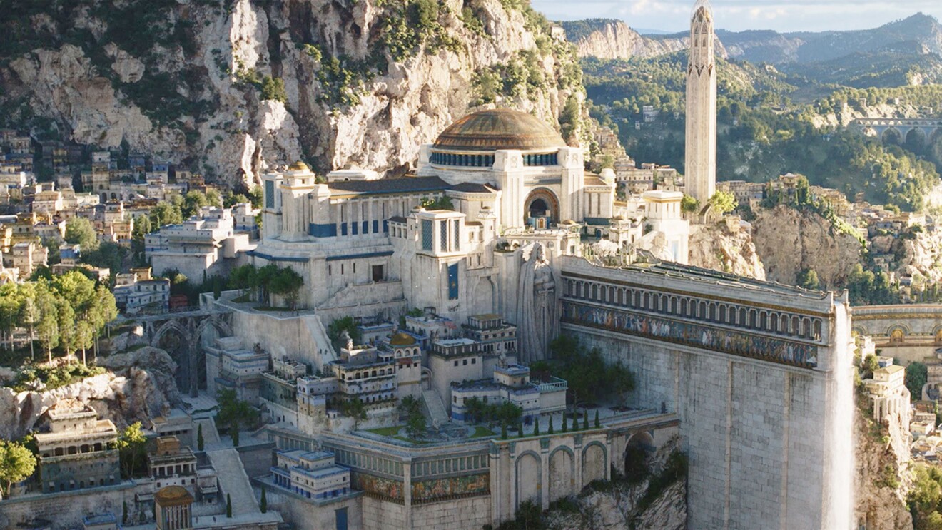 A scene from the Lord of the Rings: The Rings of Power. There is a large city on a hill with a big structure in the middle depicting a court in Numenor.