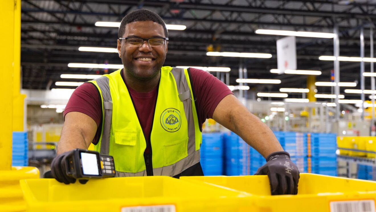 Smiling Amazon employee wearing safety vest and glasses operating scanning device in distribution center