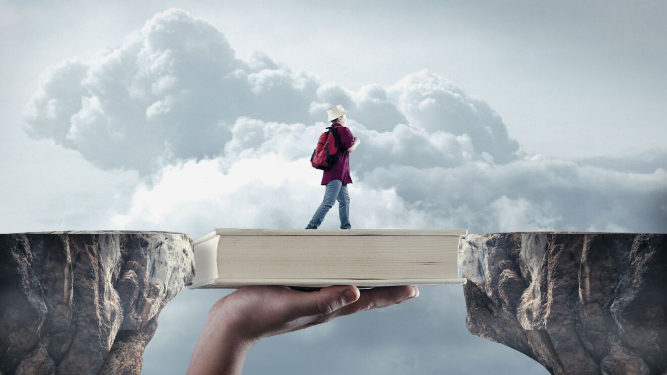 A surreal image of a person walking across cliffs bridged by a book.