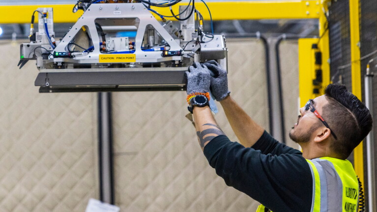 Amazon worker in safety vest adjusting robotics equipment suspended from yellow frame