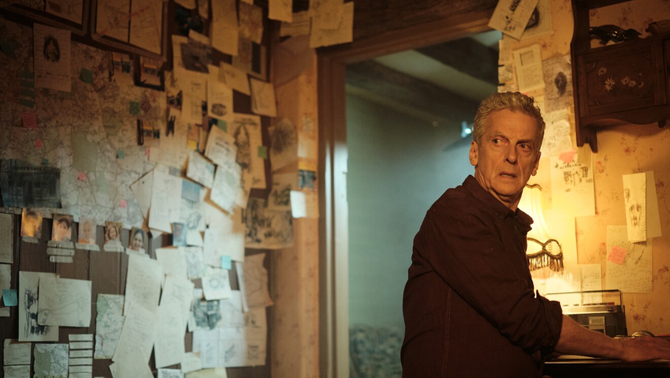 An elderly man with white hair stands in a room covered in papers