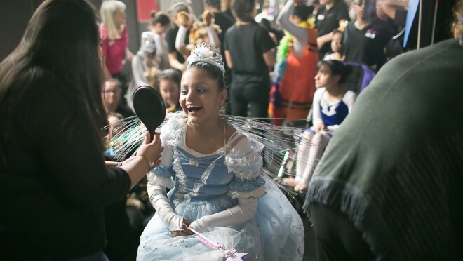 一个女孩在一个公主裙看起来小手持镜子后完成她的化妆舞蹈表演。许多其他演员在后台所示。