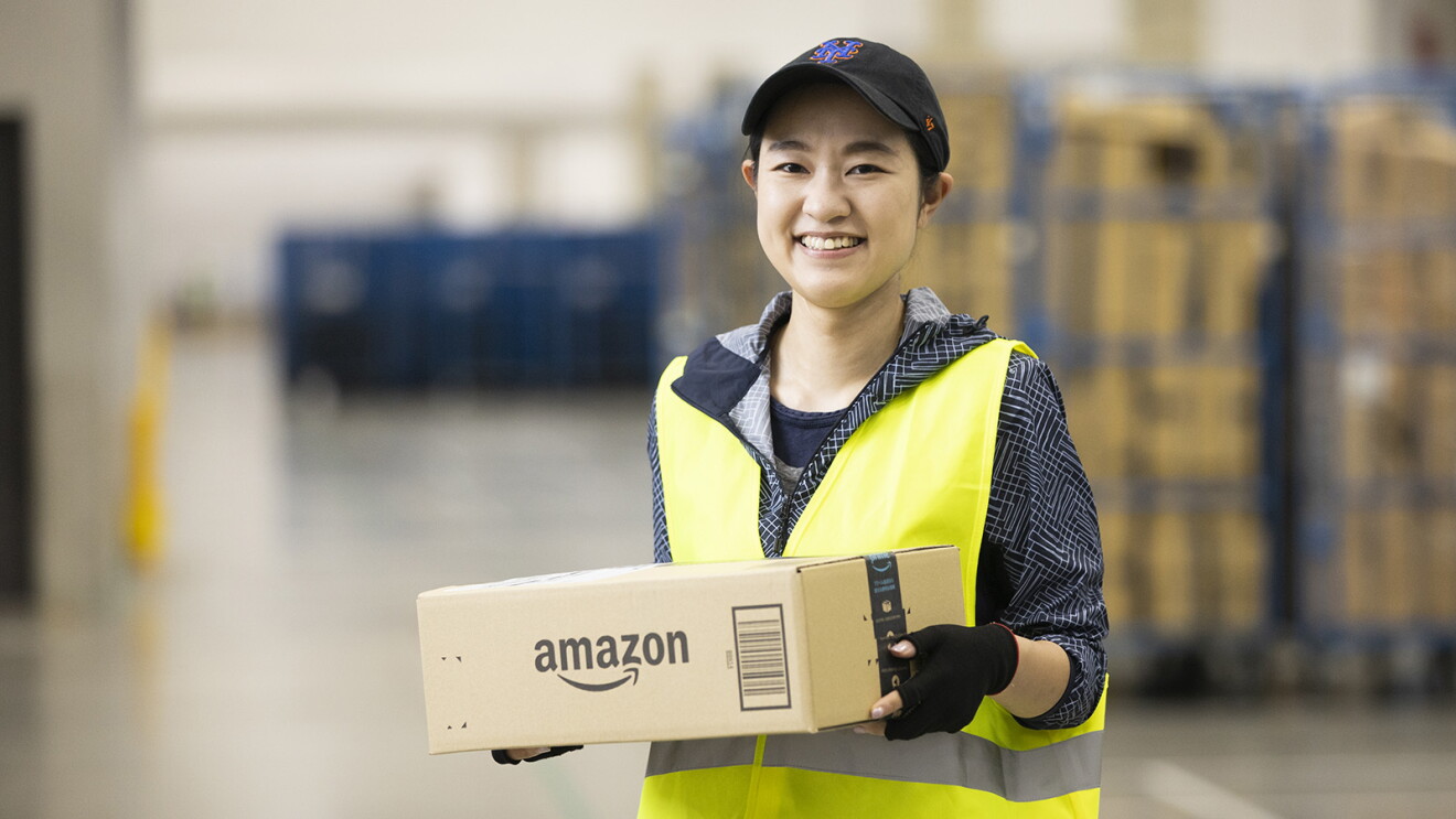 Amazonの段ボールを持つ女性。黄色い作業用ベストを着て帽子をかぶっている