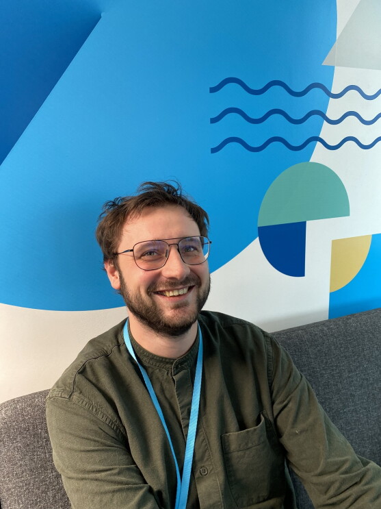 Simon Messerli sitzt auf einer Couch und lächelt in die Kamera.