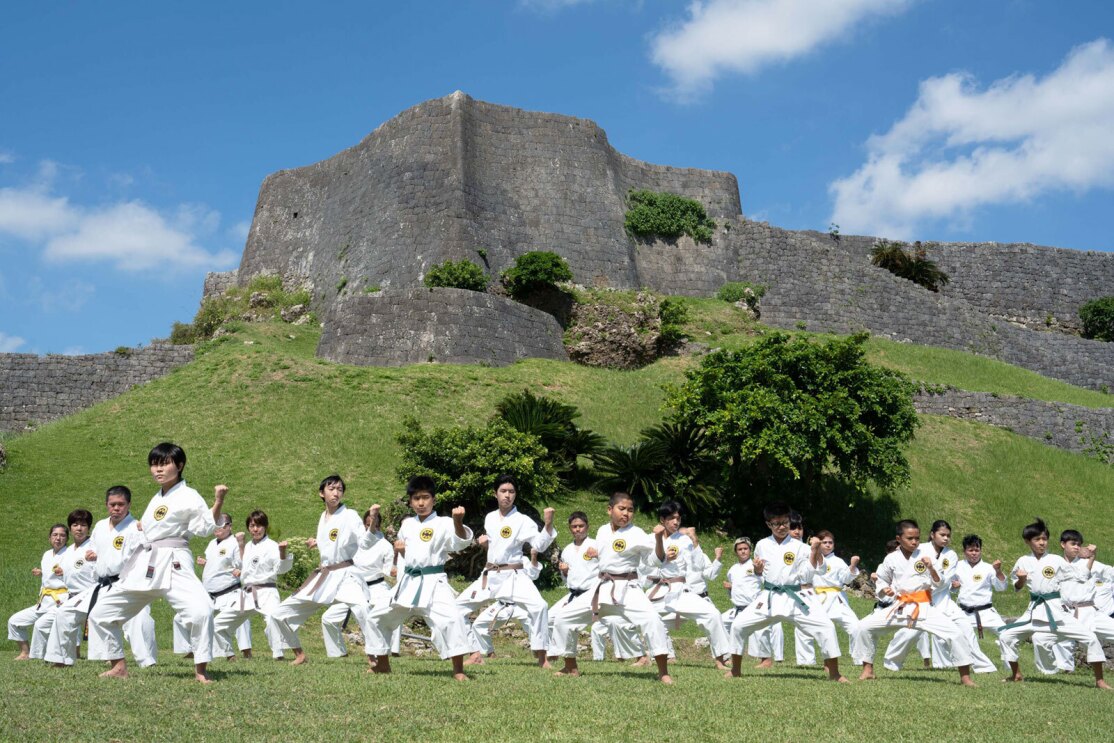 An image of a a class of kids practicing karate outdoors. 