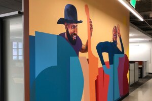 An image of a painted mural showing two people smiling and lettering at the Amazon Denver office.