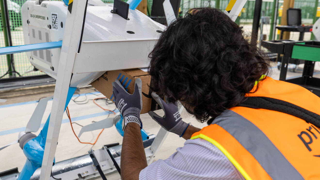Amazon worker in safety vest and gloves inserting a package into a Prime Air drone for delivery